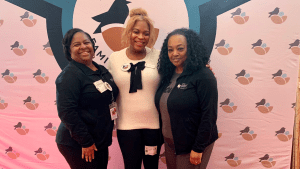Three Black women standing together, smiling in front of a colorful backdrop featuring the Maryland Family Network logo