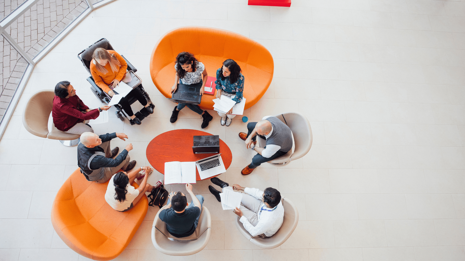A group of people in a modern seating area collaborating on documents and a laptop.